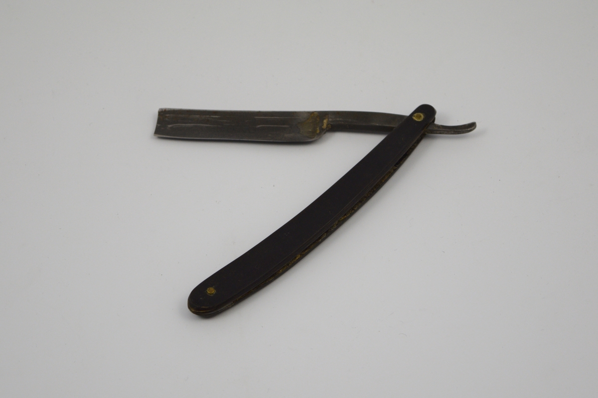 Sammenleggbar barberkniv med rett egg. Knivbladet har konisk tverrsnitt. Bladet munner ut i tynt skaft
med en krumning som holdegrep med fingeren. Skaftet er naglet fast til
kniven. Består av to deler som fungerer som beskyttelse i sammenlagt
stilling.