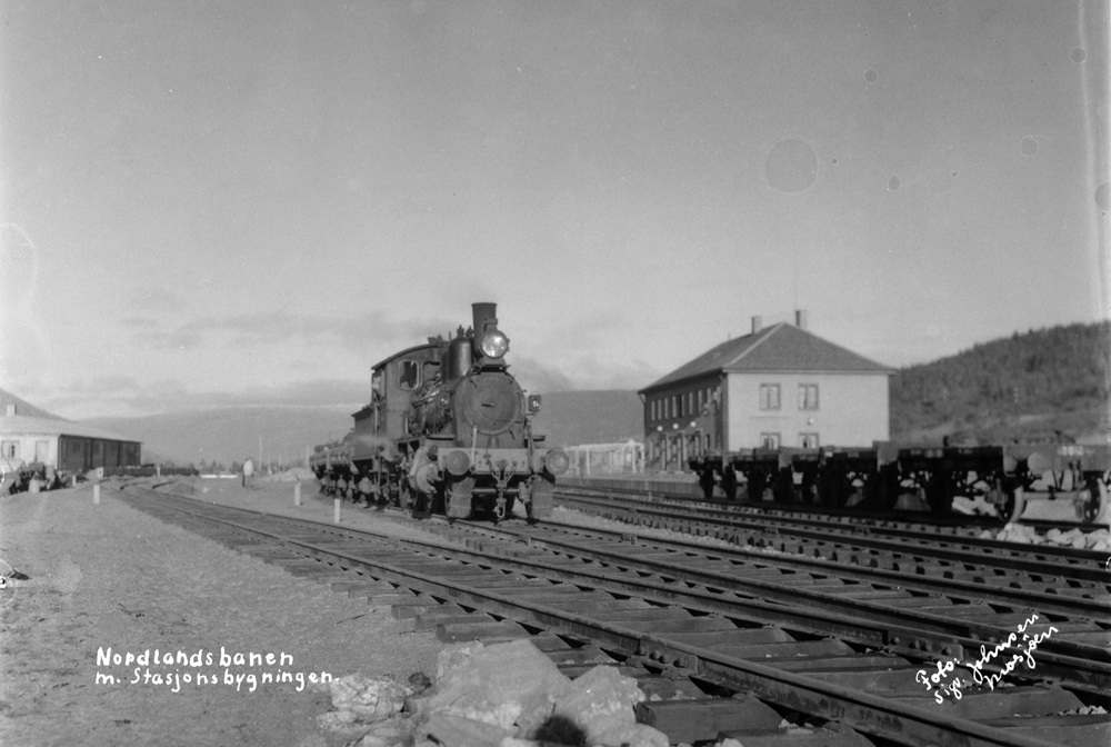 Under anleggsperioden på jernbanestasjonen.
Det første lokomotivet som kom til Mosjøen står på stasjonen. Vi ser også reisegods og stasjonen.