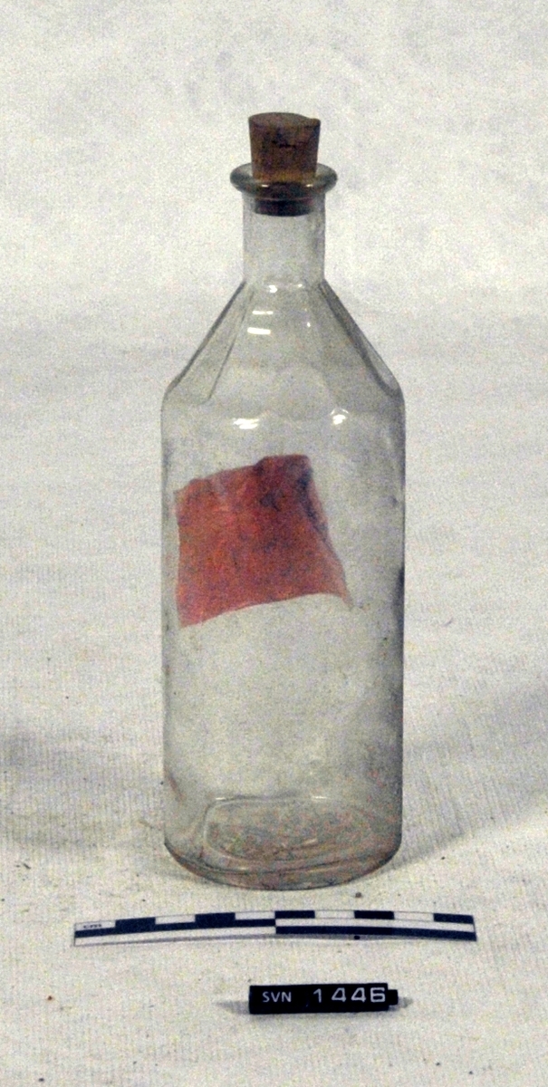 Blank flaske med kork og rosa etikett.
Etiketten er håndskrevet. Etiketten er der delvis falt av.