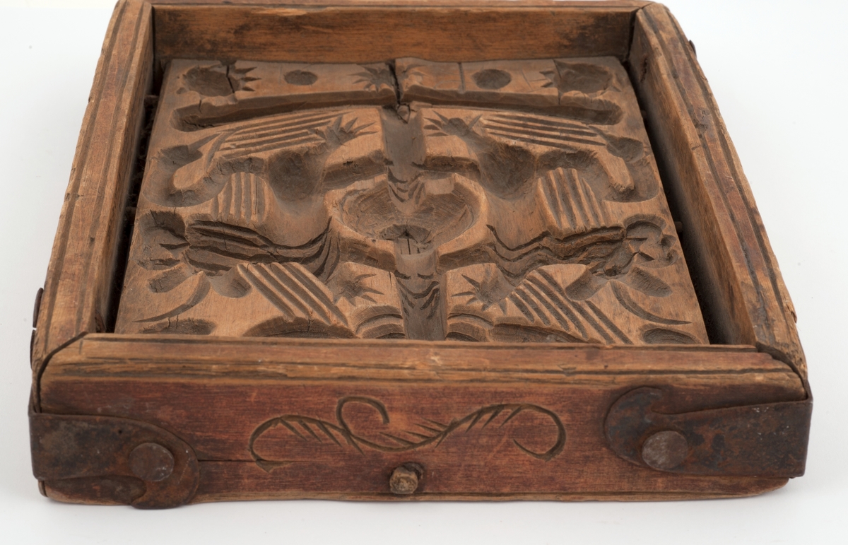 Firkantet kakeform med jernbeslag på hjørnene. Den ene siden av bunnen skåret med sol, måne, fabeldyr og et tre. Undersiden har blomster og rankedekor med 2 fugler. Litt skåret dekor på den andre siden.
Innskrift på den ene langsiden.