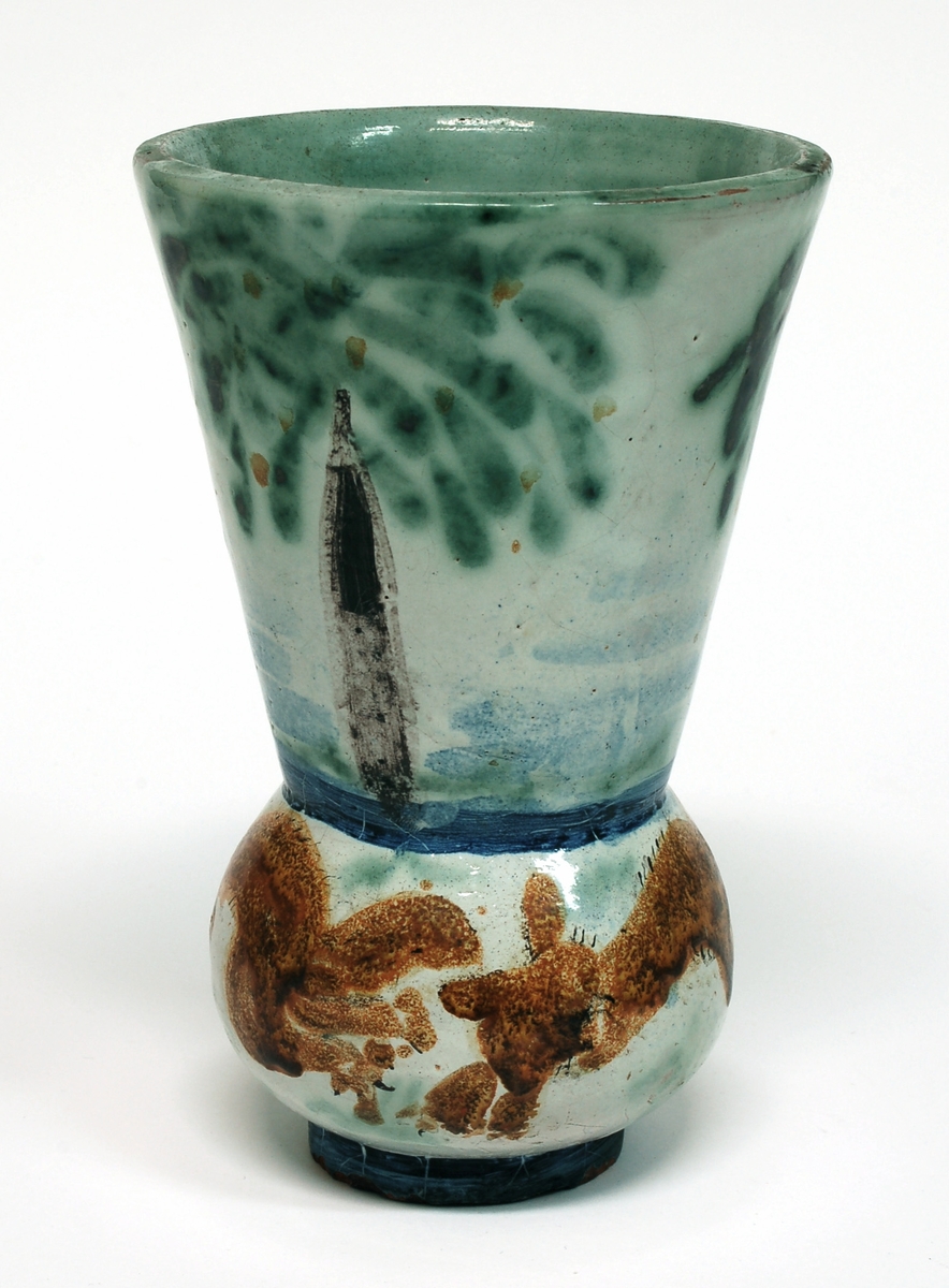 Vas, övre delen glaserad med trädmotiv i grönt, blått och brunt. Den nedre delens motiv föreställer springande ekorrar. Formgiven av Märta Willborg, 1930.
