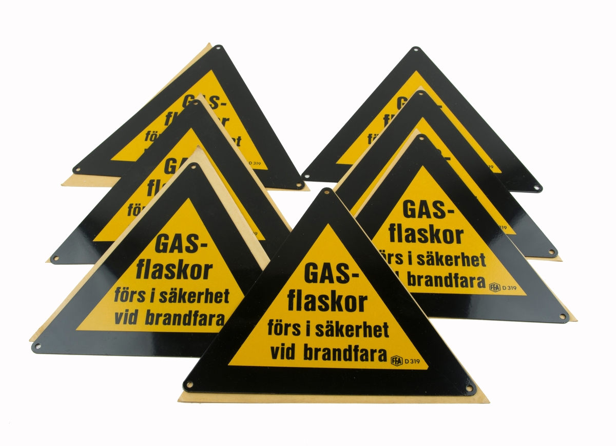 Triangelformade skyltar i bunt. Skall uppmärksamma och informera om gasflaskor. Text: Gasflaskor förs i säkerhet vid brandfara.