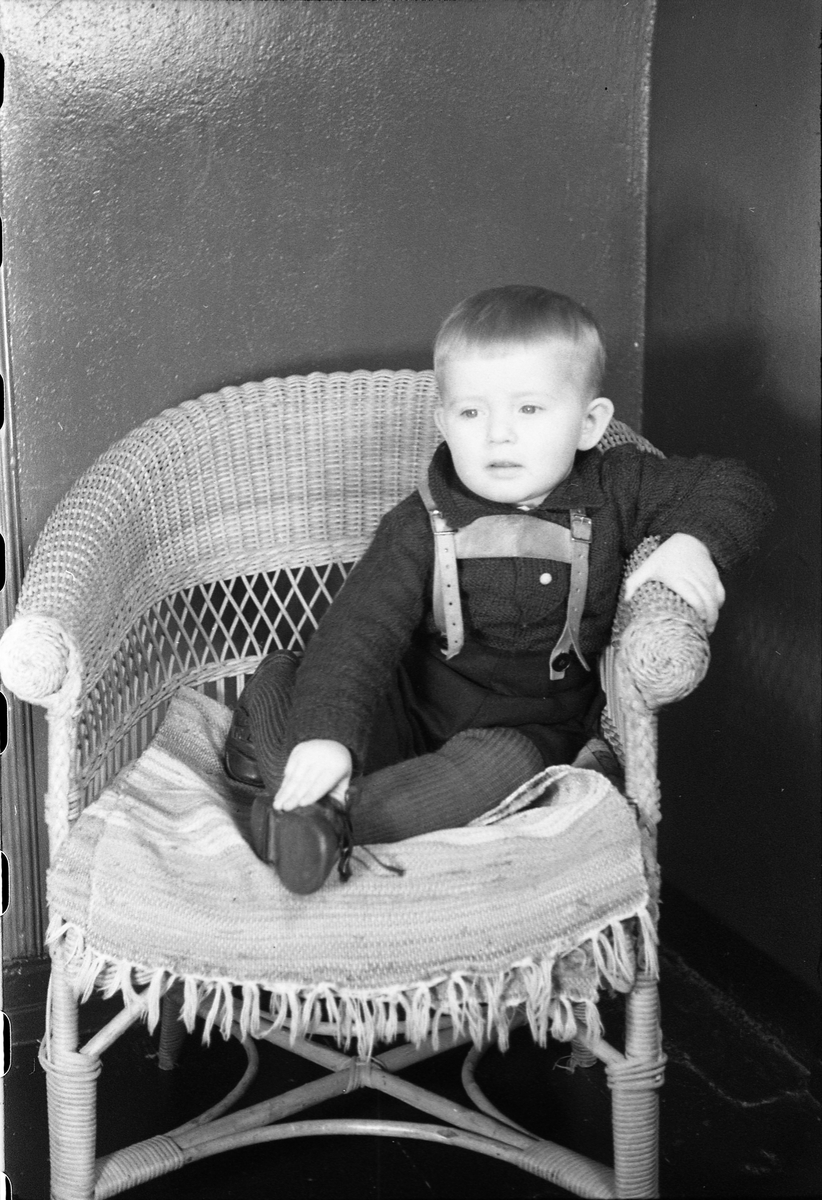 Portrett av et uidentifisert guttebarn som sitter i/står ved en kurvstol. Serie på 10 bilder.