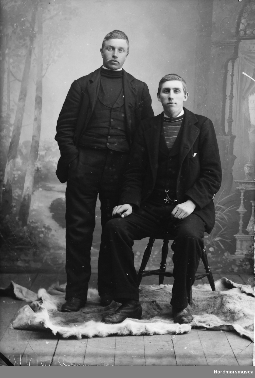 Portrett av to menn fotografert i studio. Den ene sitter på en stol. Den eine (til v.) er på portrettet SU-L01.0253.