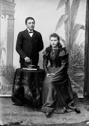 Portrett av en gutt og ei jente. Gutten står bak et rundt bo