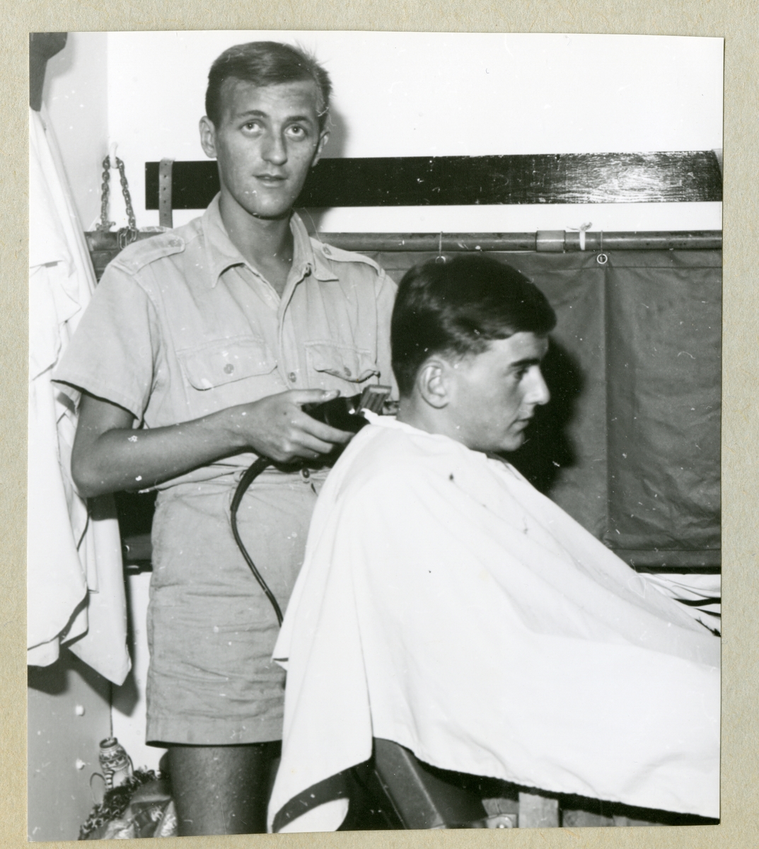 Bilden föreställer två män ombord på minfartyget Älvsnabben, där den ena får håret klippt av den andre. Bilden är tagen under långresan 1966-1967.