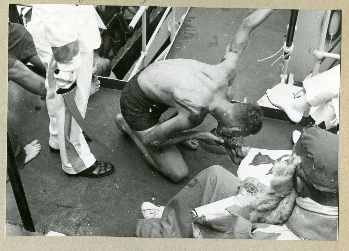 Bilden föreställer en barbröstad besättningsman ombord på minfartyget Älvsnabben som håller på att genomgå ett linjedop och får kyssa kung Neptuns fot. Bilden är tagen under fartygets långresa 1966-1967.