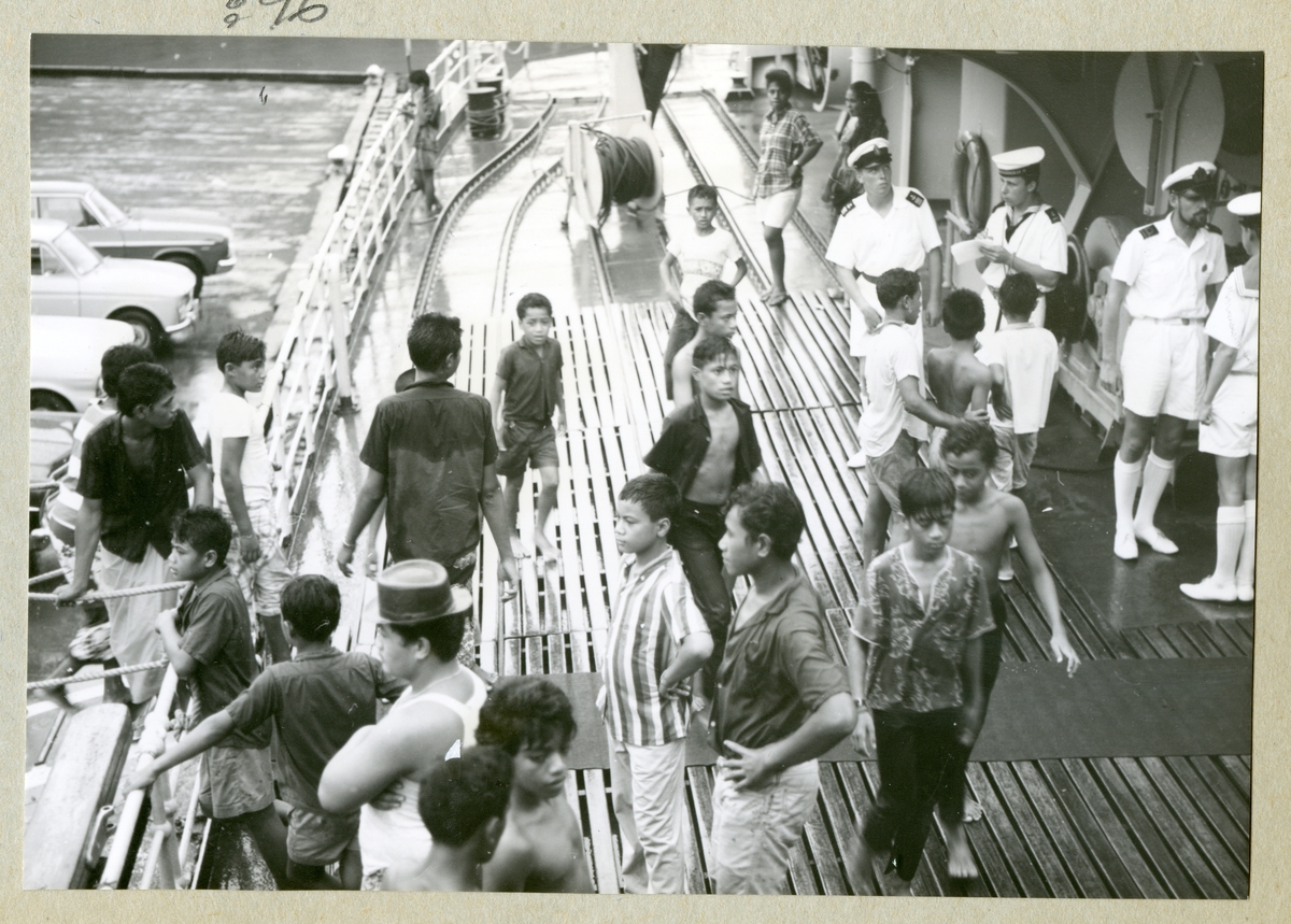 Bilden föreställer besättningsmän i vita sommaruniformer på minfartyget Älvsnabbens däck. På däck står även flera pojkar och män som är på besök på fartyget. Bilden är tagen i samband med långresan 1966-1967.