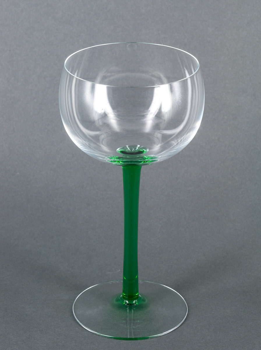 Vitvinsglas, 2 st, prov till "Nobelservisen". Tillplattat halvklotformad, ofärgad kupa. Högt, smalt, runt ben i grönt glas. Ofärgad fot. Design Gunnar Cyrén för Orrefors Glasbruk.
