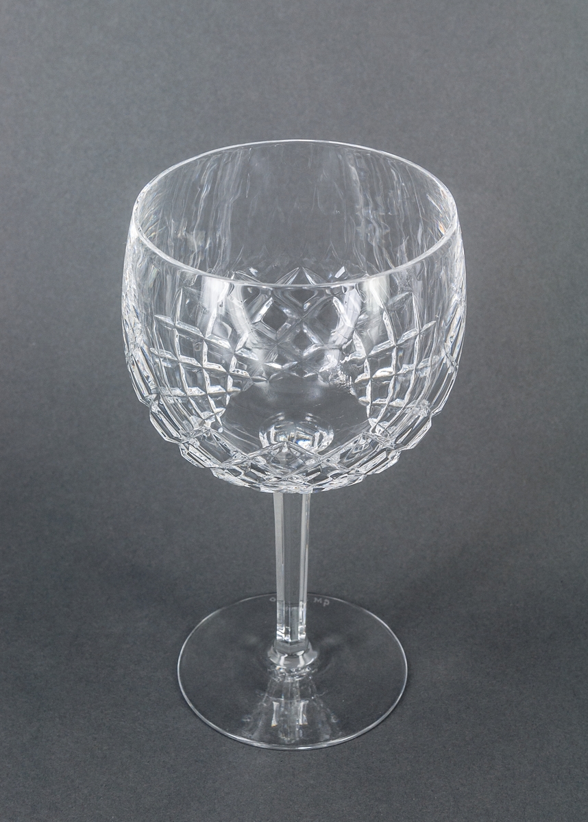 Ölglas, kristall. Halvklotformad kupa med kvadratslipningar på nedre halvan. Högt, smalt, sexkantigt ben.
GM 26858-26862 sammanhör.