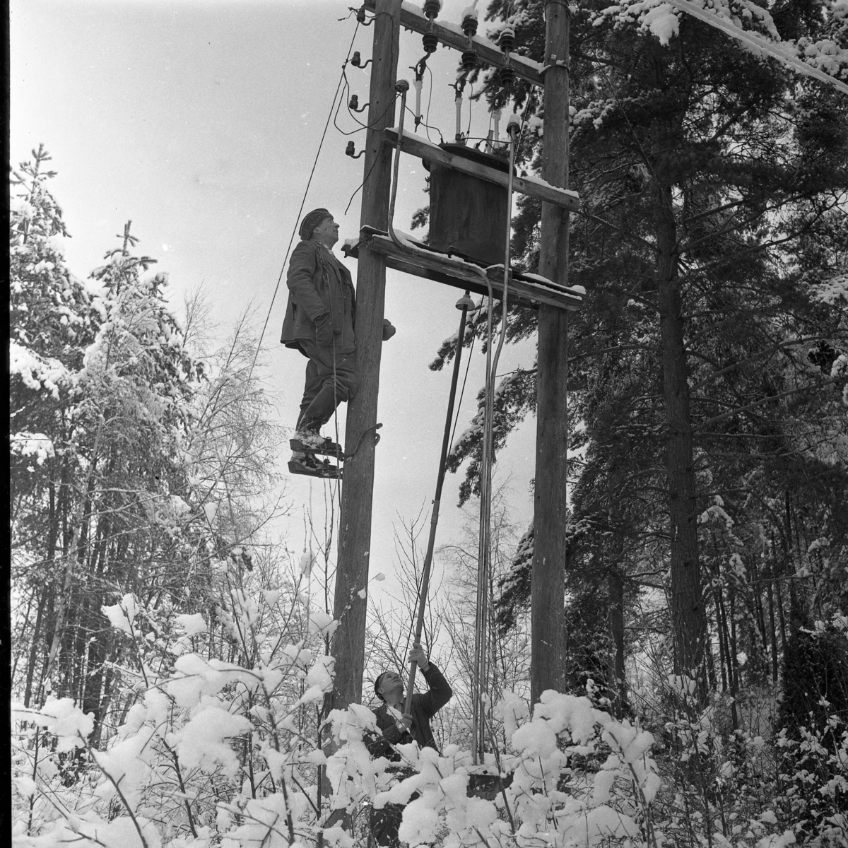 Linjemontörerna vid Gränna elverk i arbete efter "elkaos" i Grännatrakten, november 1963. Karl Pragberg på stolpen och Filip Svensson på backen.