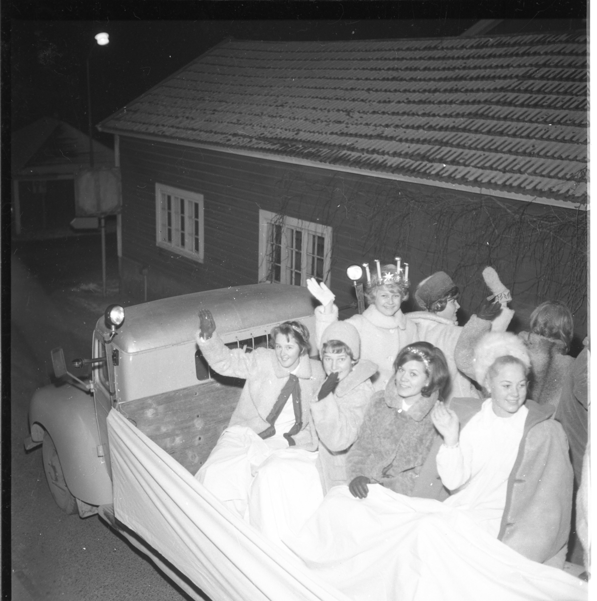 1963 års lucia med följe på P A Larssons lastbilsflak i Gränna, troligen på Hamnvägen ned mot Sjögatan. Från vänster: okänd Barbro Karlsson, Iris Gustafsson (lucia), Ewa Heldbrandt (med ryggen mot kameran) Birgitta Johansson samt Marita Wallmo.