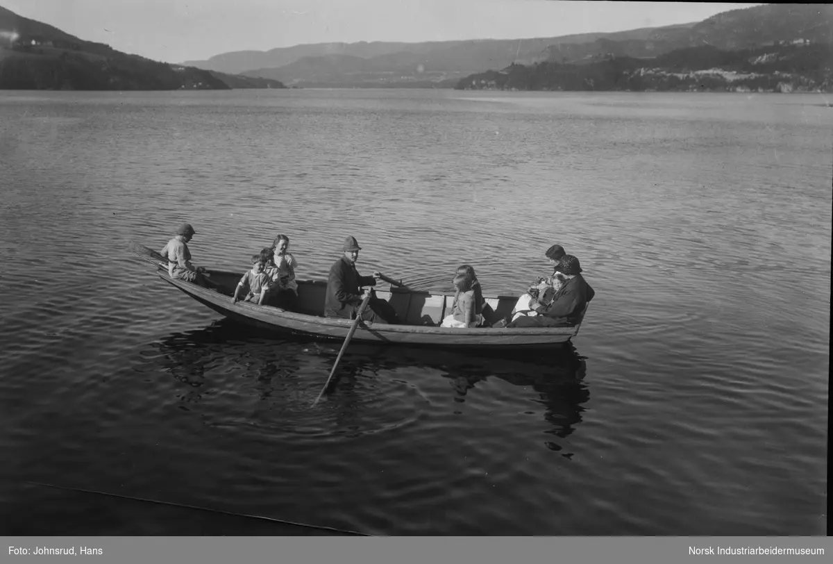 Båttur i robåt på Heddalsvatnet. Syv barn og tre voksne i båten, mann ror.