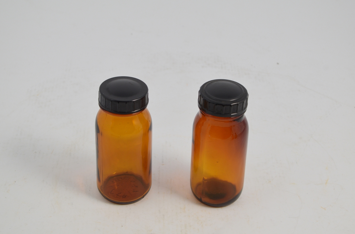 Apotekerflaske m/skrukork. Brune runde glasskrukker med sort bakelitt lokk. Glassene ble brukt til oppbevaring og slag av tabletter.