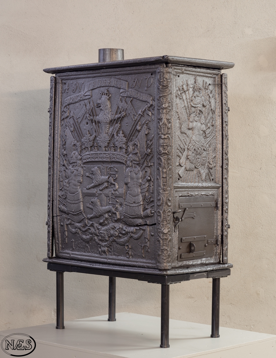 Kasseovn med ovnsdør på kortsiden og røykuttak i topplaten. Ovnen har løse skinner med bruskornamenter. På langsidene er Gyldenløves våpen omgitt av krigerske emblemer med innskrift i knekket bånd over. Øverst står det innskrevet ANNO og nederst på platen 1687. På kortsiden er det øverst krigerske emblemer og nederst den norske løve omkranset av brusk-kartusj.