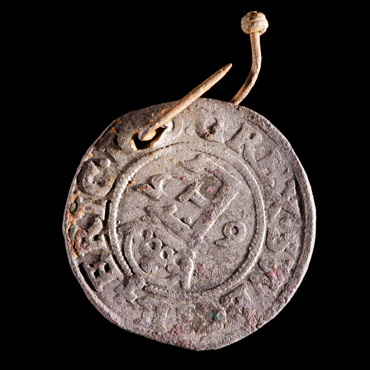 Mynt. 1/2 öre myntat av Erik XIV 1565. Hål med vidsittande knappnål av järn. Åtsida med krönt E och frånsida med Vasavapnet.