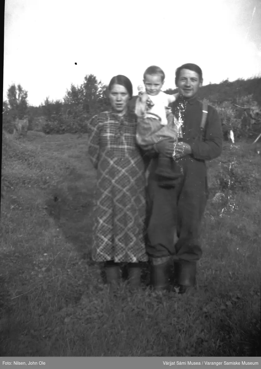Gruppebilde utendørs. En kvinne og en mann som holder et lite barn. Barnet holde ren dukke. Mannen er Johan (Jonte) Roska. Muligens Fuoitnjárga / Bunes på 1940 tallet.