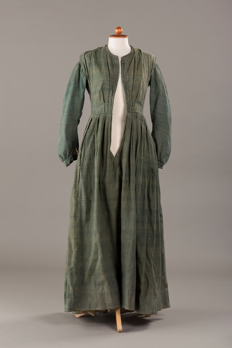 Form: Trangt liv med legg foran, skjørtet sydd med legg i livet.  God vidde i skjørtet, lange armer. Fem hekter i livet mangler.