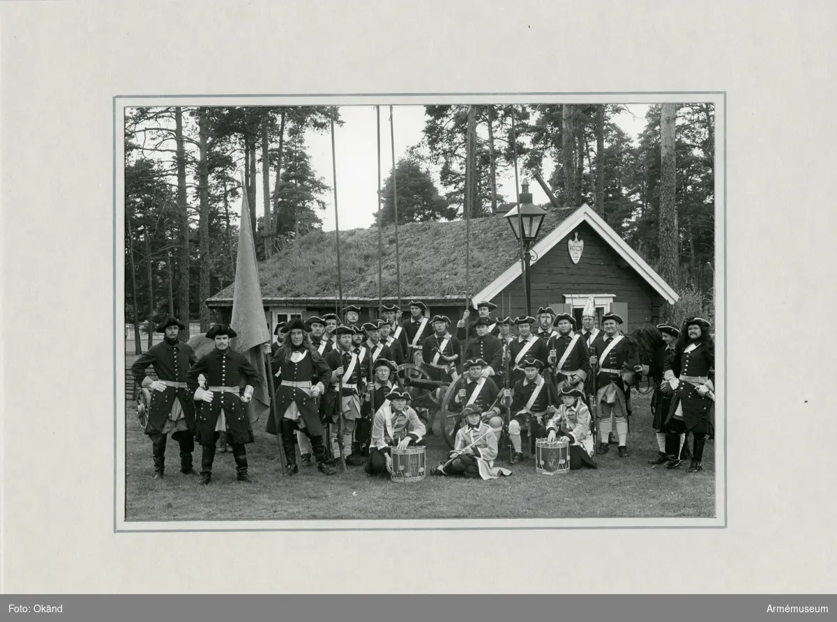Grupporträtt av Smålands Karoliner framför soldattorp.
