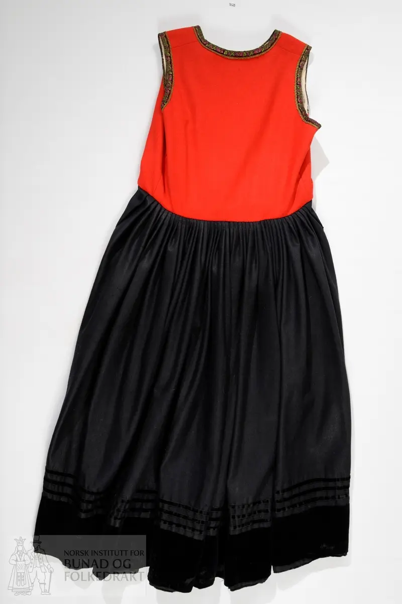 Liv sauma av raud ullkypert, lett valka. Fora med ubleika bomullslerret.
Ermhole, rundt hals og opning framme er kanta med blomstermønstra fleirfarga fløyelsband med svært avslitt fløyel. Innanfor kantingar er det påsett eit smalt metallband.
Etter framkantane er det påsett 3 borer på kvar side, dei to øverste litt breiare enn dei fire nederste, alle har eit skåleforma lauv festa i midten. På framsida av den kurva delen er det fem ulike stempel: 63 i eit sirkelforma stempel, truleg årstalsstempel. Månadsstempel: 6 over M i rektangelforma stempel. Mesterstempel i bølgeforma ramme LAR, Lorentz Christopher Angel Reimers, fekk borgarskap i Bergen i 1832. Lødighetsstempel 13 1/3. Trapesforma stempel med 7 prikkar, Bergens bystempel.
Lukking framme med to metallhekter på kvar side.
Heile livet er sauma på maskin. Kanting er sauma for hand. 
Livet sauma på stakken for hand. 
Stakken er av heimevove ullerret, blåsvart. Splittopning midt framme. Samansett av 5 rette høgder med jare i begge sider, alle høgder. Faldelagt oppe med eit glatt felt framme mot splitt. Høgdene er sauma saman med maskin. 
Nedkant: 3 svarte smale sillkefløyelsband, nedanfor dei eit påsett stoffstykke av svart bomullsfløyel. Dette stoffet er ein hengefald, ikkje sauma fast i nedkant.
Nedkanten er skonna på innsida med eit lerretsvove mohairstoff av mørk grøn farge. Sauma på med maskin. I nedkant av skonninga er det påsett eit blåsvart kosteband sauma på for hand.
Kanten på linninga er av svart bomullssateng. Er bretta dobbelt og sauma på for hand på begge sider