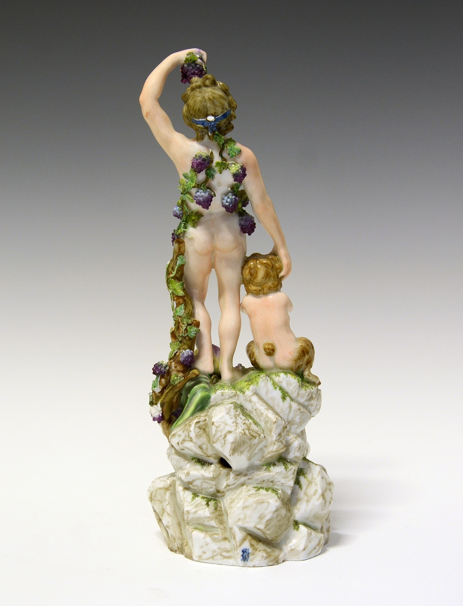 Dionysos kryster druer, og spiser fra en drueklase, Pan sittende ved hans føtter, begge på en immitert bergsokkel.