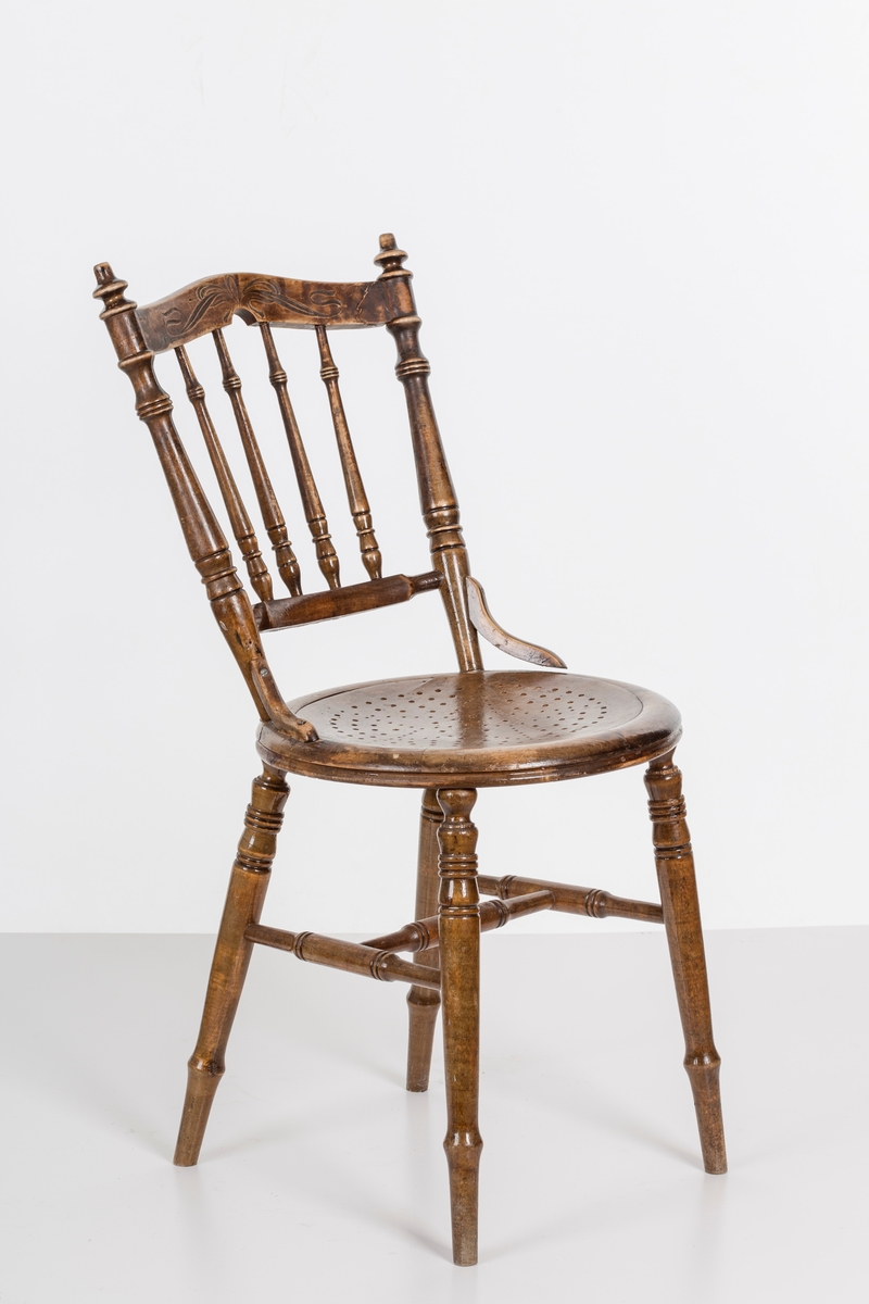 Stol i lakket treverk. Rundt stolsete med hullemønster. Rygg som er svakt buet med spiler og mønster. Dreide ben og spiler i rygg.