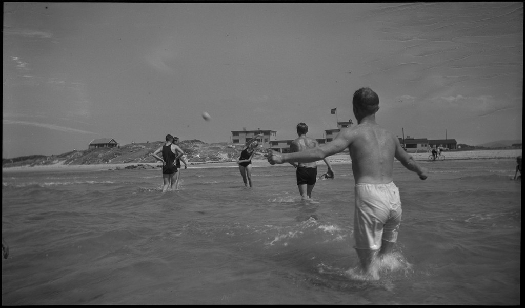 En stor vennegjeng i lystig lag på stranda på Sola. De har trommer og trekkspill og leker i vannet og på land med og uten ball. Sola strandhotell ligger i bakgrunnen. Tor Johannessen og Harald Bergsaker er på bilde nr. 14 og 18.