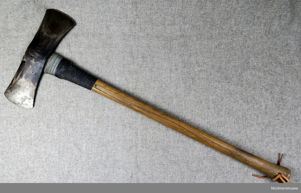 Ømed ståltks med nokså langt og tynt skaft. Øksebladet er dobbeltsidig. Skaftet er reparert med ståltråd og lerretsteip.
På enden av skaftet er ein stor E innskoren.