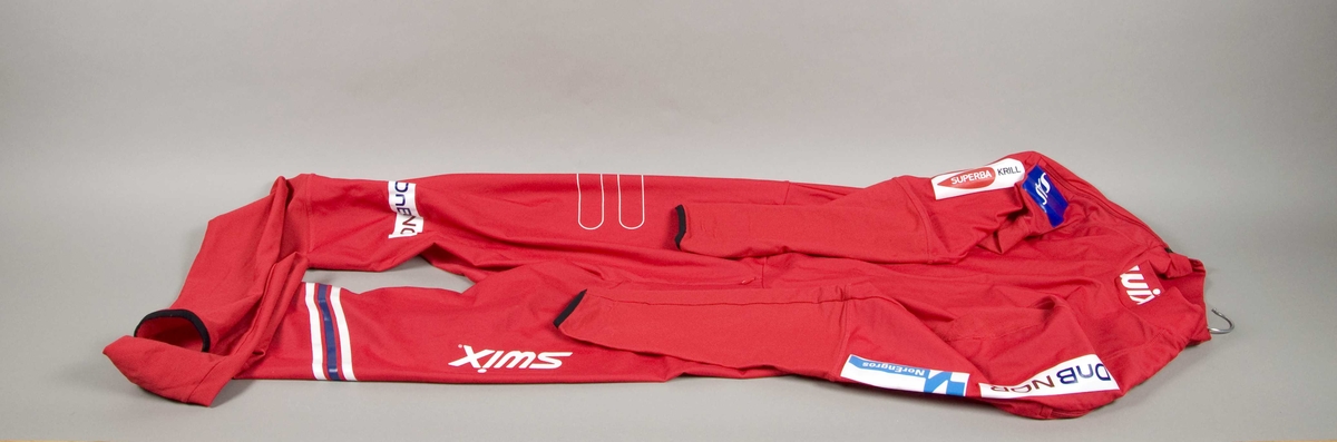 Rød langrennsdress med hvite og blåe striper. På dressen er det flere laminerte logoer for forskjellige sponsorer.
