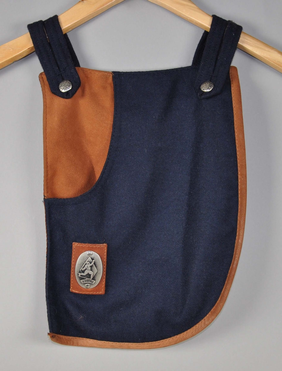 Taske i mørkblått ullstoff,dyp lomme i front kantet med skinn,glidelåslomme sydd i foret på baksiden.