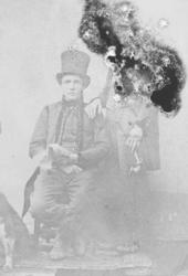 Mann sitter i ført folkedrakt og flosshatt med en mann som s