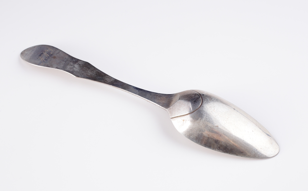 Matsked i silver, 
Fiolmodell, slät med ås. Ägarinitialer: "N.N.S." på baksidan av skaftet. Stämplar på ovansidan av skaftet.