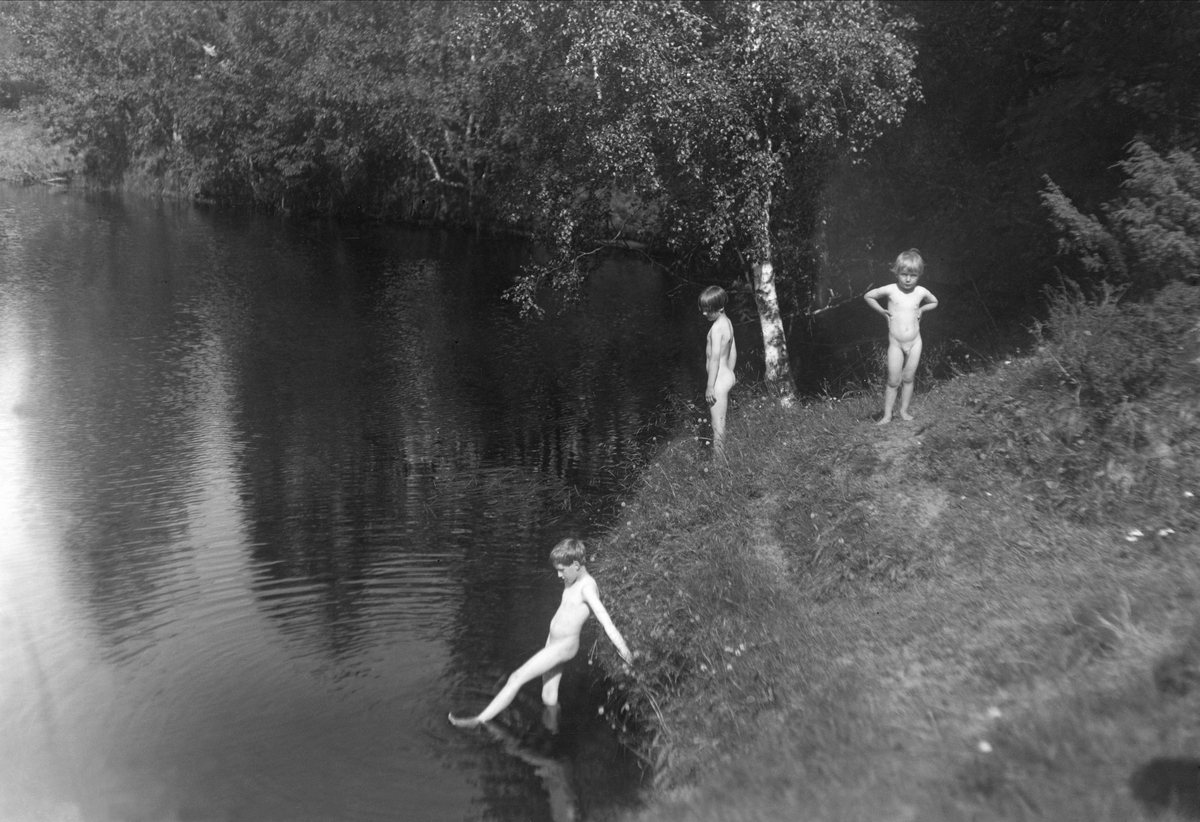 Vid badet. Fotografens barn Folke (född 1921), Margot (född 1923) och Rolf Renström (född 1928) står isolskenet i sluttningen ner mot älven. I bakgrunden lummiga träd.