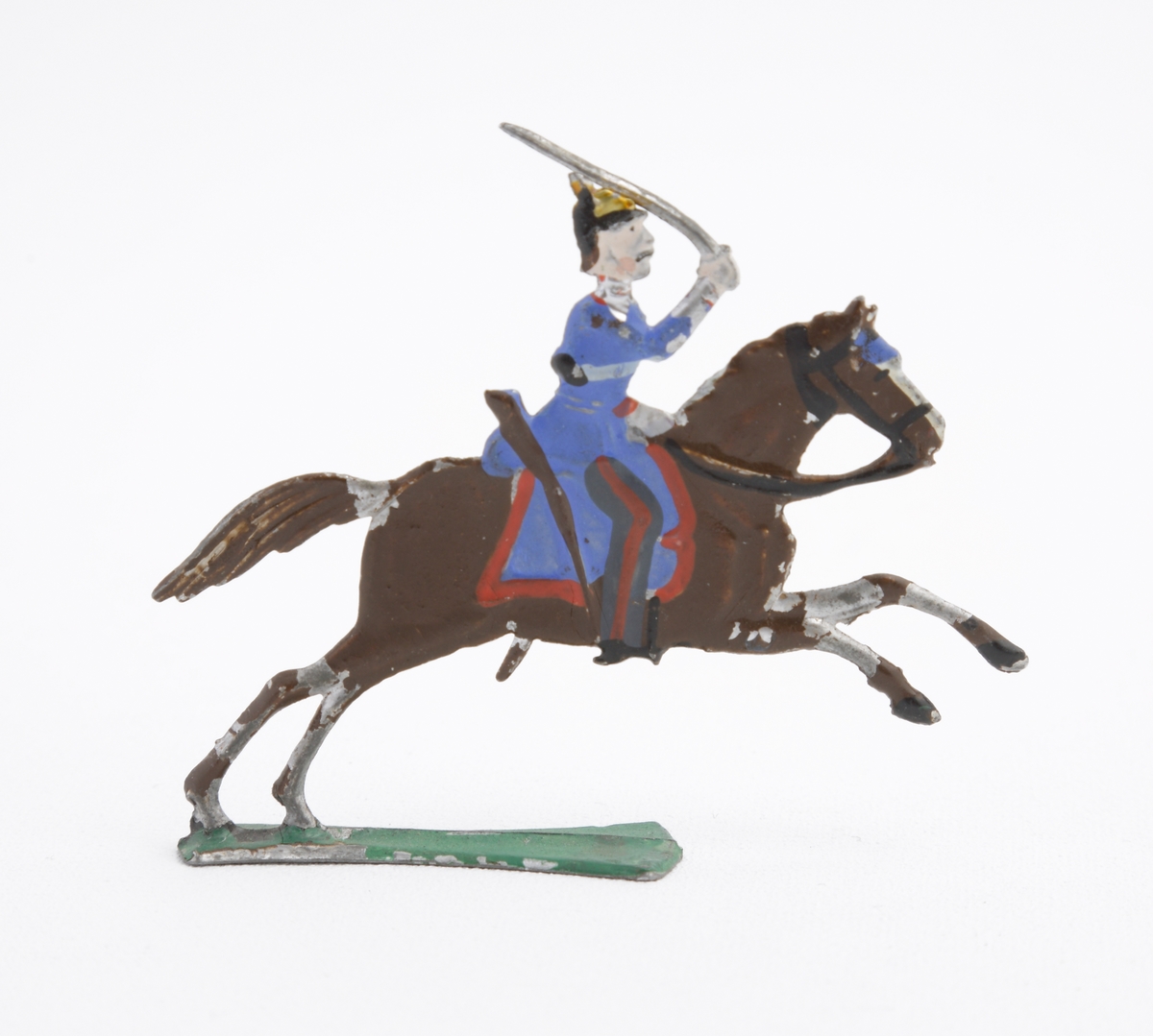 Ryttare till häst i blå uniform med dragen sabel. Han är även utrustad med koppel och pickelhuva. Sadeln är blå med röda kanter. Hästen brun på grön platta.
Inskrivet i huvudkatalog 1963.