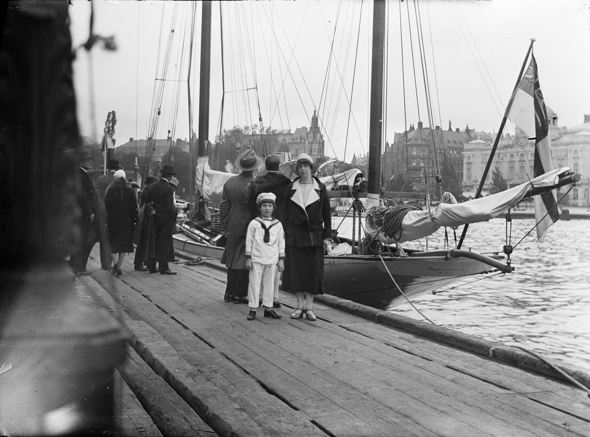 Kvinna och pojke bland folk som betraktar segelbåt vid Nybroviken, Nybroplan med Kungliga Dramatiska Teatern i bakgrunden, Stockholm tidigast 1908