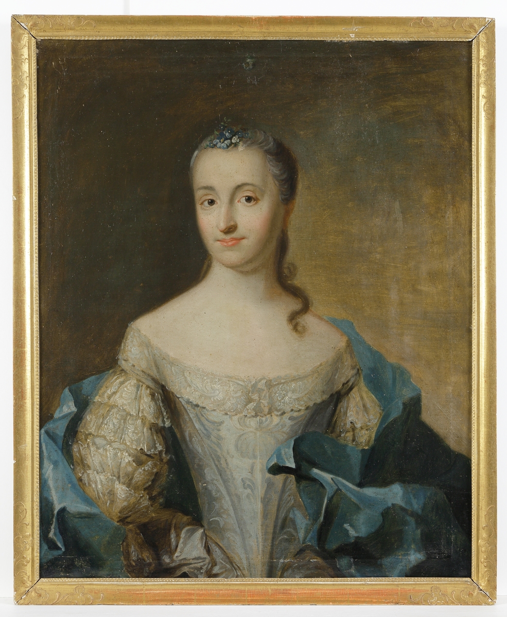 Oljemålning.
Porträtt av kvinna i ljusblå klänning med spetsärmar och blå mantel. Midjebild, halvprofil.
Ej signerat. 
Förgylld ram, med blad- och bärdekor i hörnen.