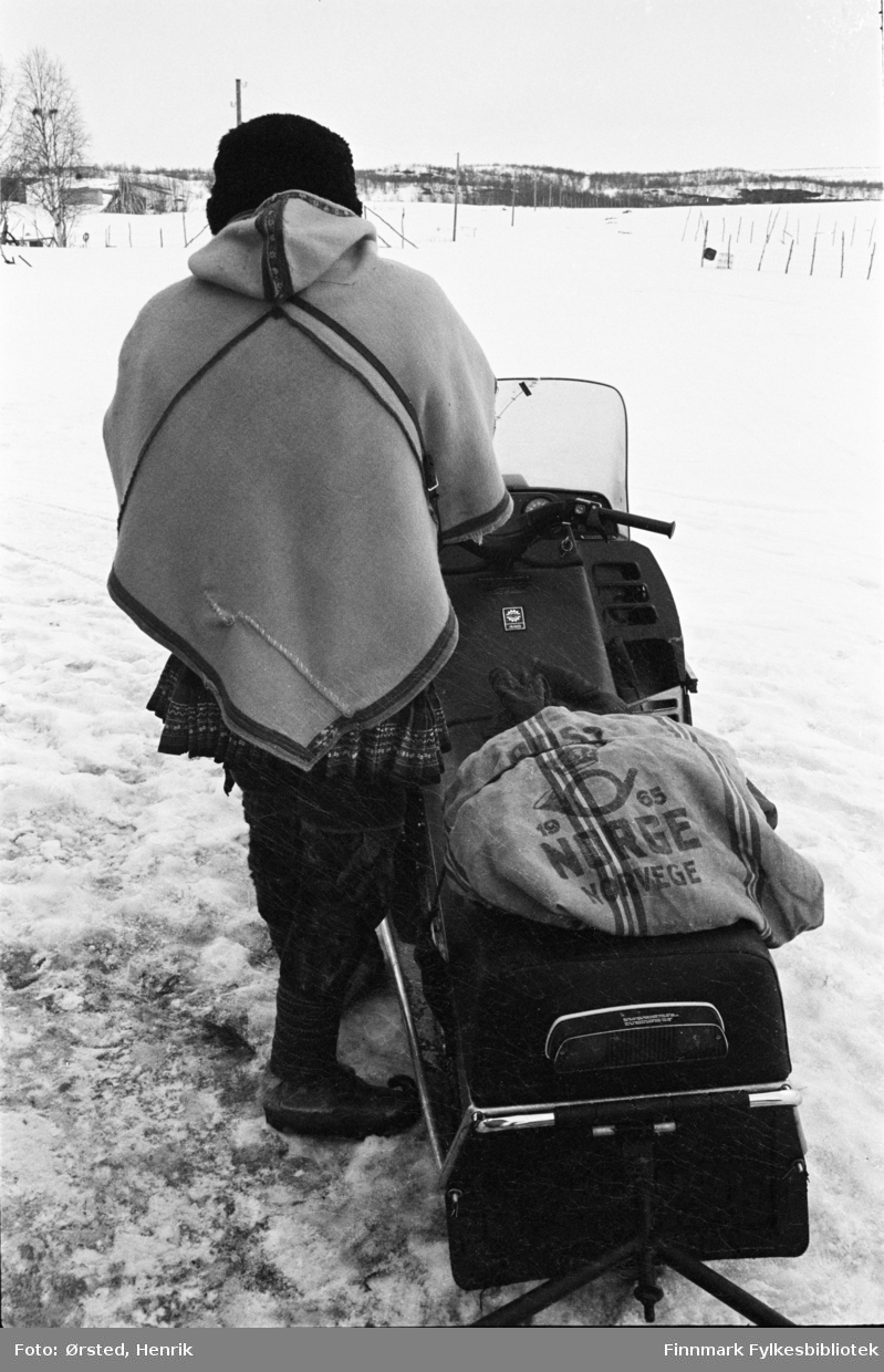 Postfører Mathis Mathisen Buljo, bedre kjent som "Post-Mathis" i samiske kretser, fotografert på snøskuteren ute på Finnmarksvidda. Postsekken er bundet fast på skuteren.  Mathis har på seg luhkka utenpå kofta for å beskytte seg mot kulda. 

Fotograf Henrik Ørsteds bilder er tatt langs den 30 mil lange postruta som strakk seg fra Mieronjavre poståpneri til Náhpolsáiva, videre til Bavtajohka, innover til øvre Anárjohka nasjonalpark som grenser til Finland – og ruta dekket nærmere 30 reindriftsenheter. Ørsted fulgte «Post-Mathis», Mathis Mathisen Buljo som dekket et imponerende område med omtrent 30.000 dyr og reingjetere som stadig var ute i terrenget og i forflytning. Dette var landets lengste postrute og postlevering under krevende vær- og føreforhold var beregnet til 2 dager. Bildene gir et unikt innblikk i samisk reindriftskultur på 1970-tallet. Fotograf Henrik Ørsted har donert ca. 1800 negativer og lysbilder til Finnmark Fylkesbibliotek i 2010.