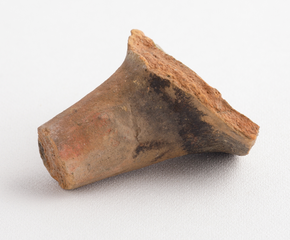 Koniskt ben av yngre rödgods, sannolikt till en trefotsgryta. Benet är avbrutet. Kärlbukens insida har brungul till olivgrön glasyr. Tillverkad i södra Skandinavien.