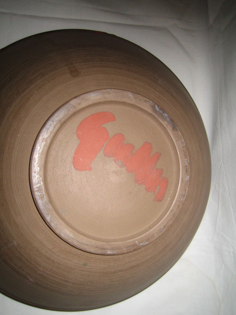 Rund skål i naturfärgad keramik på utsidan och svart och röd glasyr på insidan.