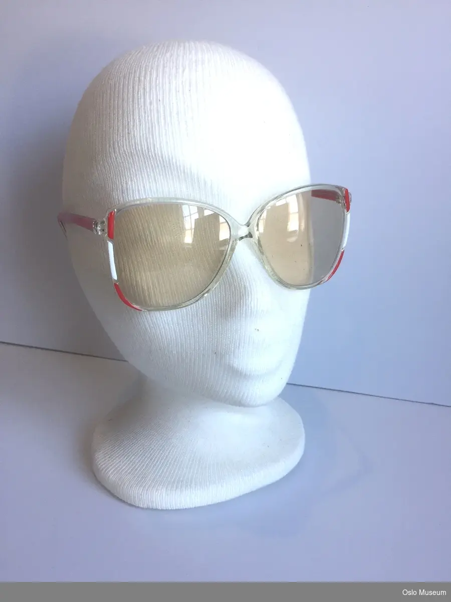 Damesolbriller med innfatning i gjennomsiktig plastmateriale med rød og hvit dekor.