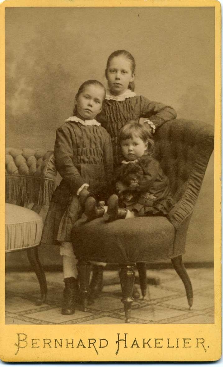Kabinettsfotografi: tre okända flickor varav den minsta sittande i en emma.
