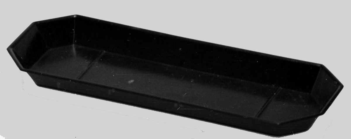 En avlang svart skål av plast eller bakelitt. Skålen er avrundet i hver ende.