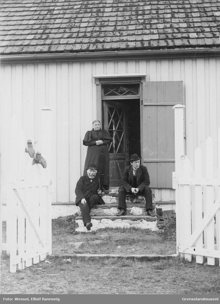 På prestegårdstrappa i Grense Jakobselv, våren 1896. Lærer og kirkesanger Anders Nilsen Tokle og sokneprest Emil Stang Lund sitter på trappa. Fru Kristofa Tokle står bak.