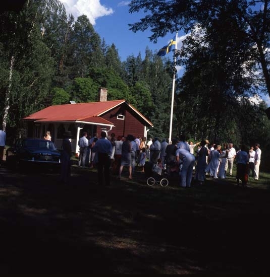 Bröllop i Ängratörn, juli 2001. Det är sommar och vigseln förrättas utomhus. Gästerna har samlats utanför Albert Vikstens torp där flaggan är hissad.