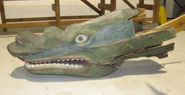 Alligator/krokodil med ett huvud och två sidor, som omslutit stäven. Öppen käft med sammanhängande tandrader och rombformade fjäll på ryggen. Målad i grönt och gult. Krokodilen består av flera delar, varav stora delar tidigare varit rejält angripna av röta. Huvud och höger sida är bäst bevarade.