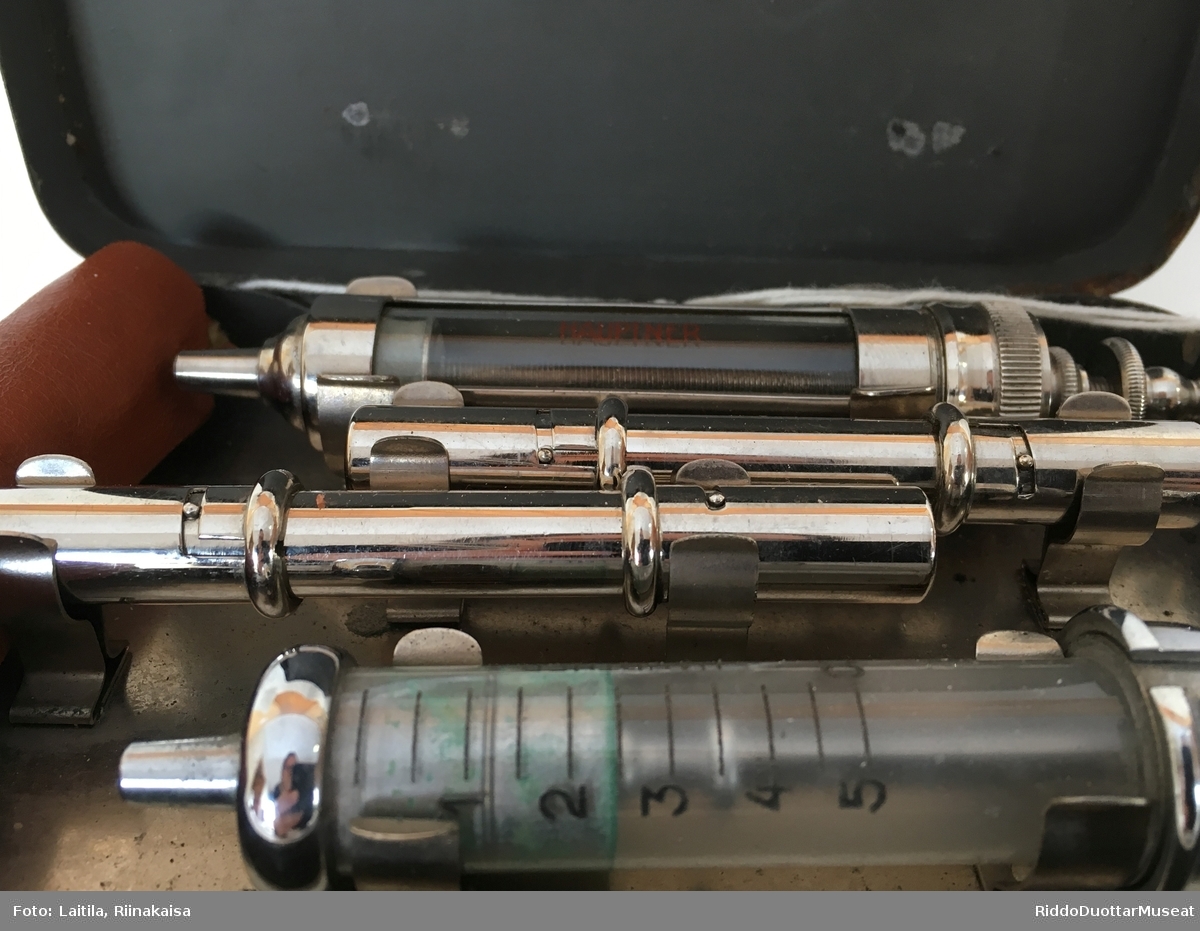 Førstehjelpsskrin. Metalleske med to sprøyter, nåler og metallbeholdere. Varemerke på sprøyter Hauptner.