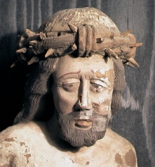 Törnekrönt Kristusfigur av ljust lövträ med djup urholkning på baksidan. Höger arm ligger mot bröstet, vänster arm är avbruten. Hårets lockar är ristade i kritgrunden.