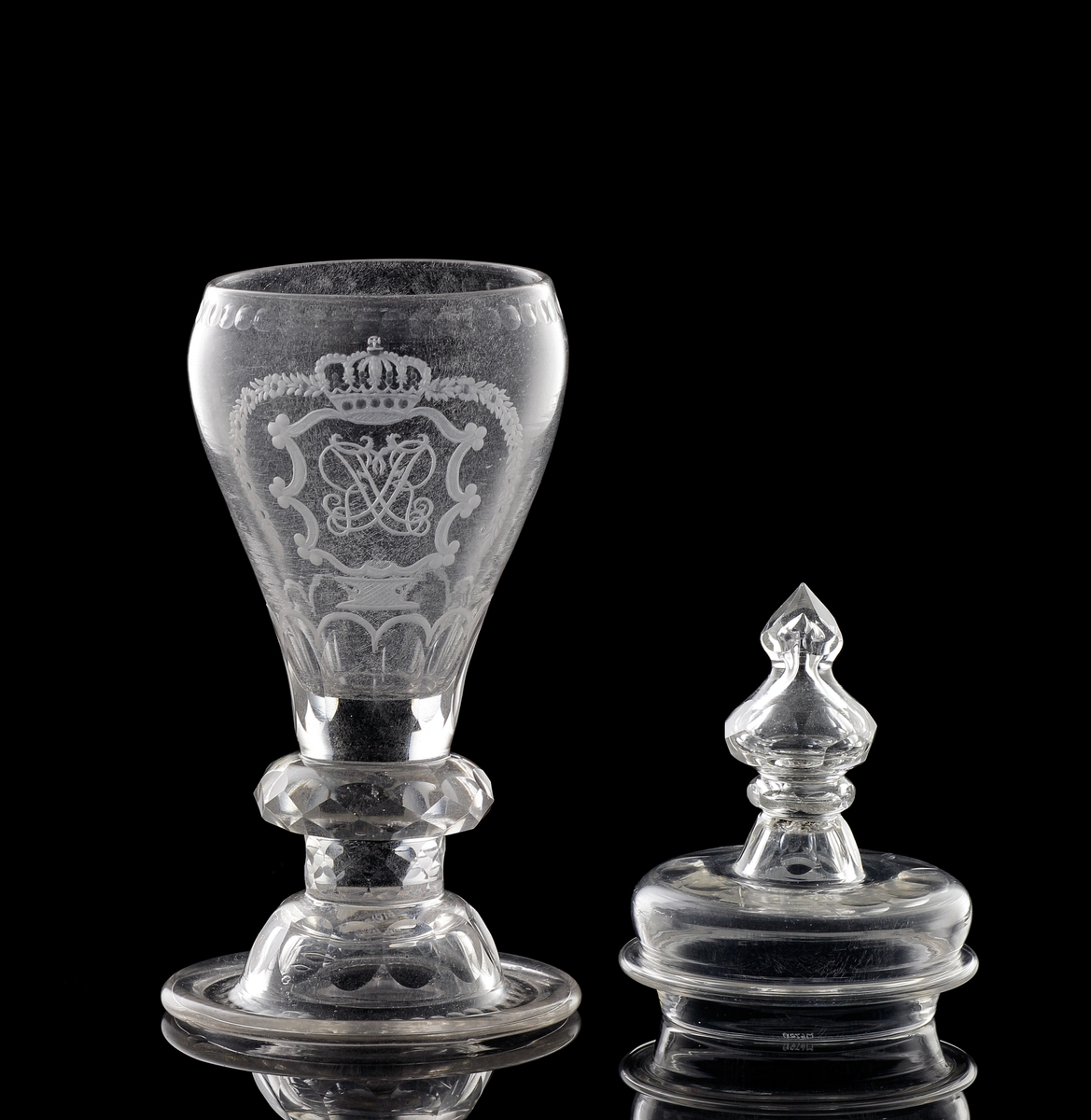 Pokal av glas, med lock. 
Slipat och graverat mönster med kungligt spegelmonogram: "FR"* i kartusch under krona.

*"FR" (Fredericus Rex= Fredrik I av Sverige, reg. 1720-1751).