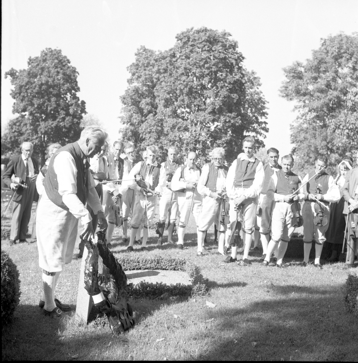 Riksspeleman Gustaf Wetter, för Södermanlands spelmanslag, lägger en krans på "Blinde Jannes" grav, Gränna kyrkogård, i juli 1964.