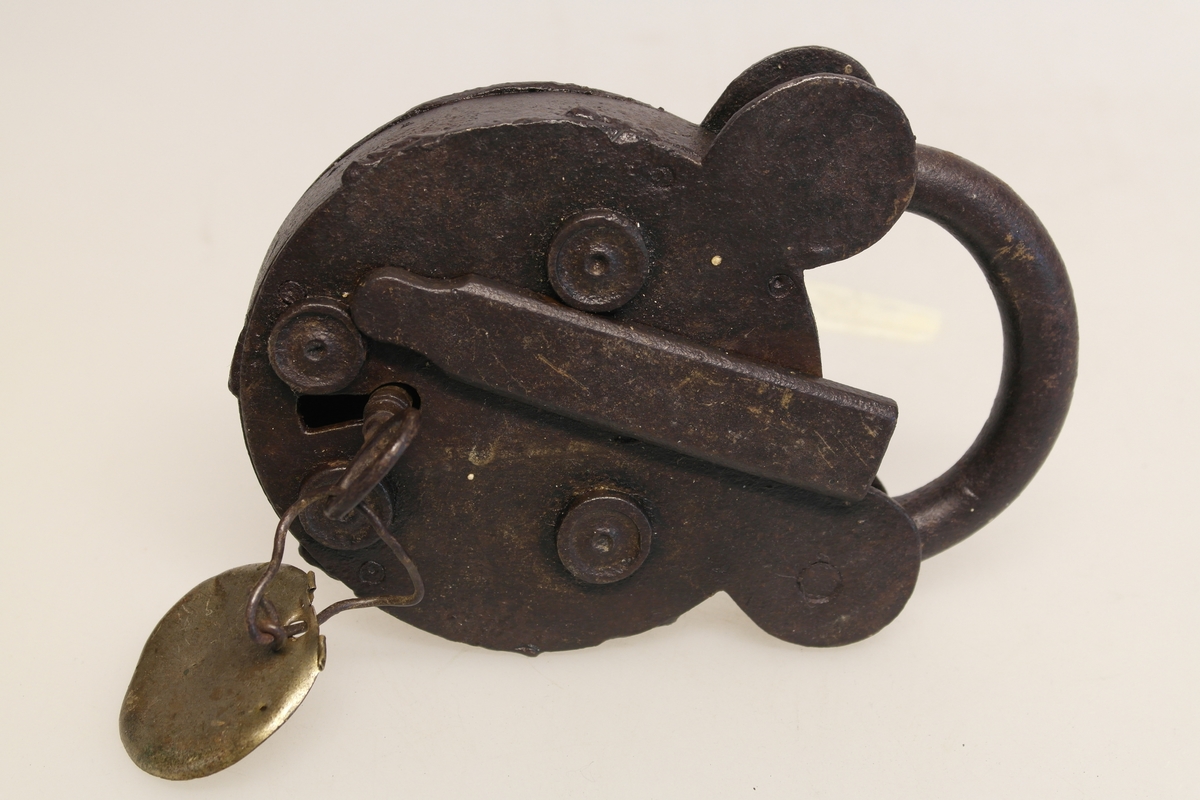 Hengelås (A) i jern. Sirkelform med bøyle. Nøkkelen står i. En rund messingplate (B) er festet til nøkkelen.